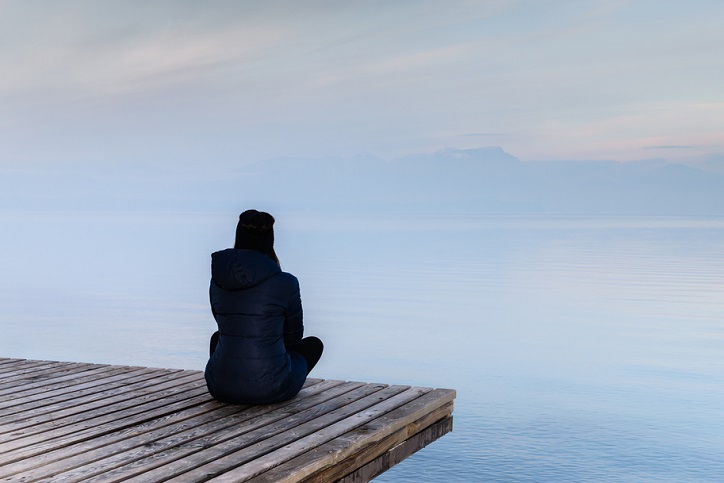 A woman sitting on a dock staring out at the water
