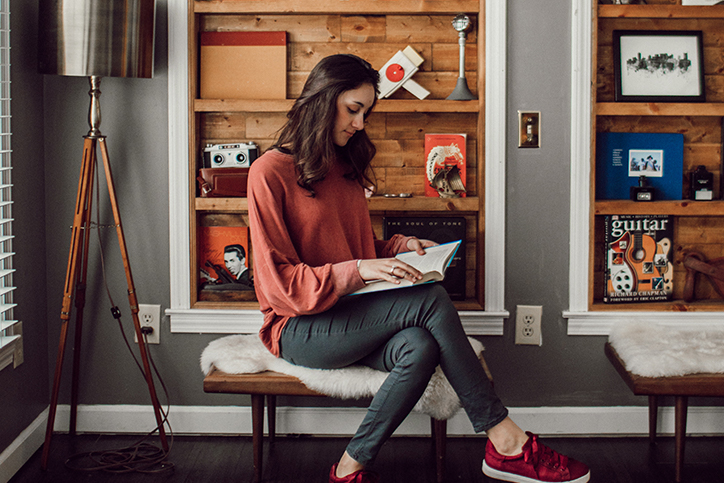 A woman sitting next to a shelf reading