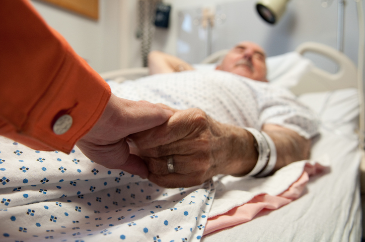 A woman holds a terminally ill man's hand.