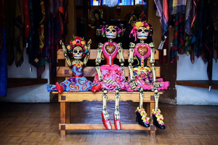 Three Dia de los Muertos skeleton puppets sitting on a bench