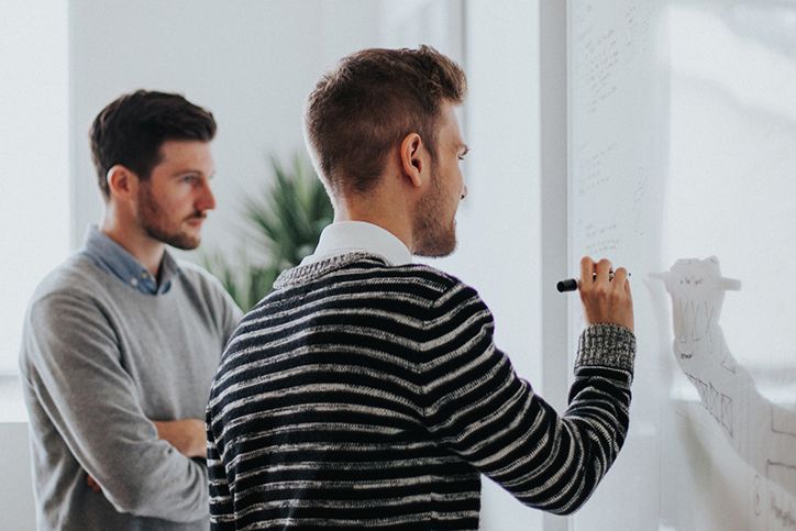 Two men write their marketing plans on a whiteboard.