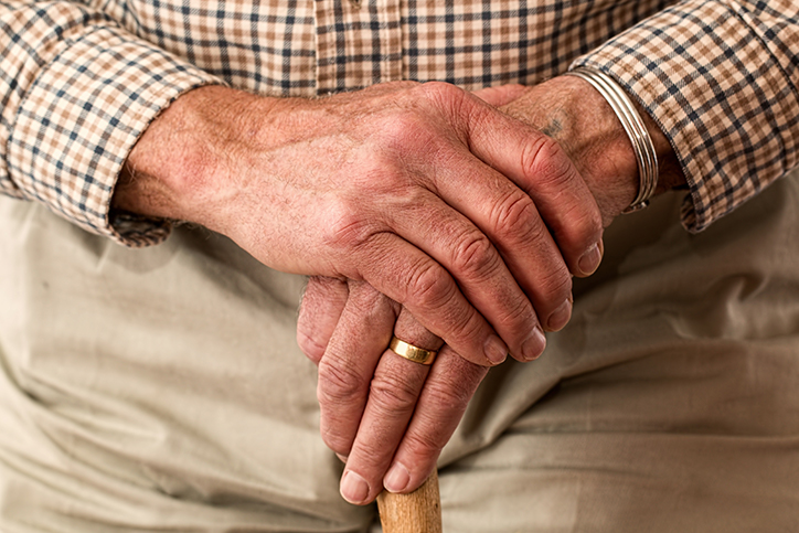 Old hands holding a walking cane