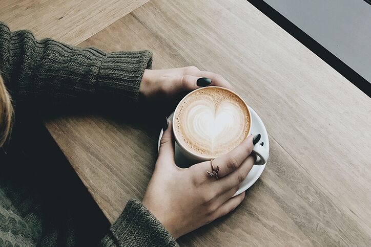 A woman with a cup of coffee with a cream heart in it
