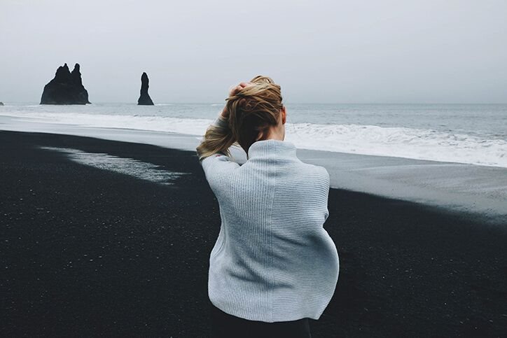 A woman sitting on a cold beach in a sweater