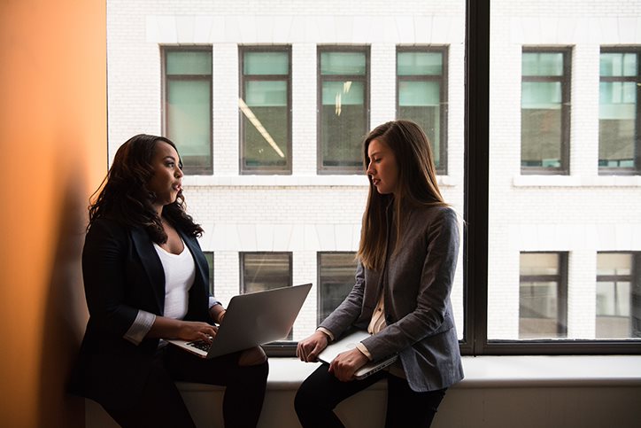 Two female professionals having a conversation near an office window