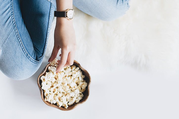 Hand taking popcorn from a small wooden bowl