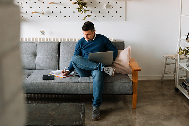 Man sitting on a couch at home with laptop and notebook